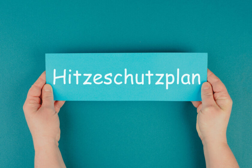 Auf dem Bild ist ein Schild mit der Aufschrift Hitzeschutzplan zu sehen. Der Hintergrund ist blau.