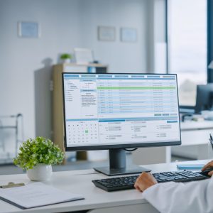 Experienced Female Medical Doctor Wearing White Coat Working on Personal Computer in a Health Clinic. Medical Health Care Professional Working with Test Results, Patient Treatment Planning.