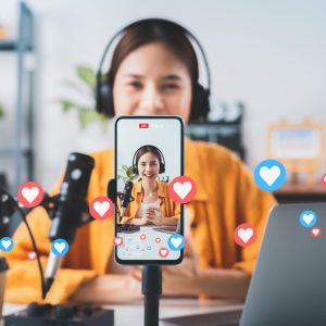 Vlogger live streaming podcast review on social media, Young Asian woman use microphones wear headphones with laptop record video. Content creator concept.
