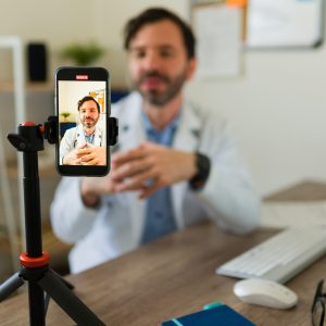 Hispanic doctor streaming using his smartphone or filming an online video for his patients or social media while at the office