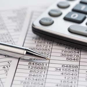 Ein Taschenrechner liegt auf den Zahlen einer Bilanz uns Statistik. Symbolphoto für Umsatz, Gewinn und Kosten.